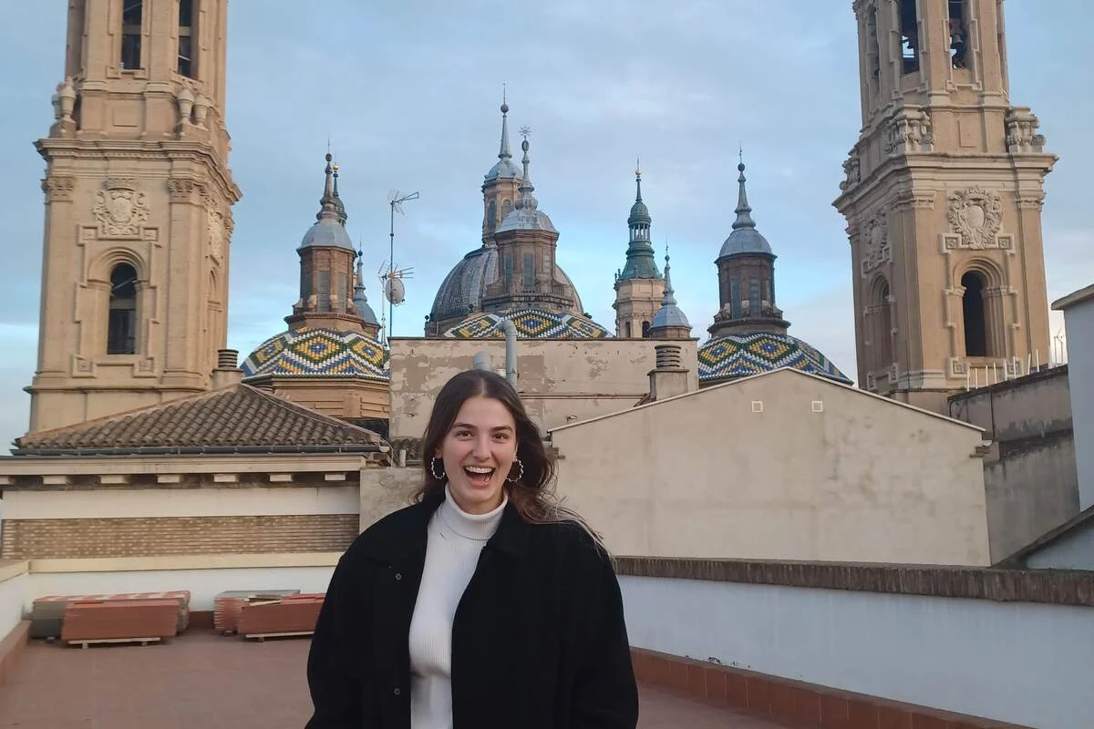 Woman smiling on a rooftop with historic, domed towers and colorful tile roofs in the background.