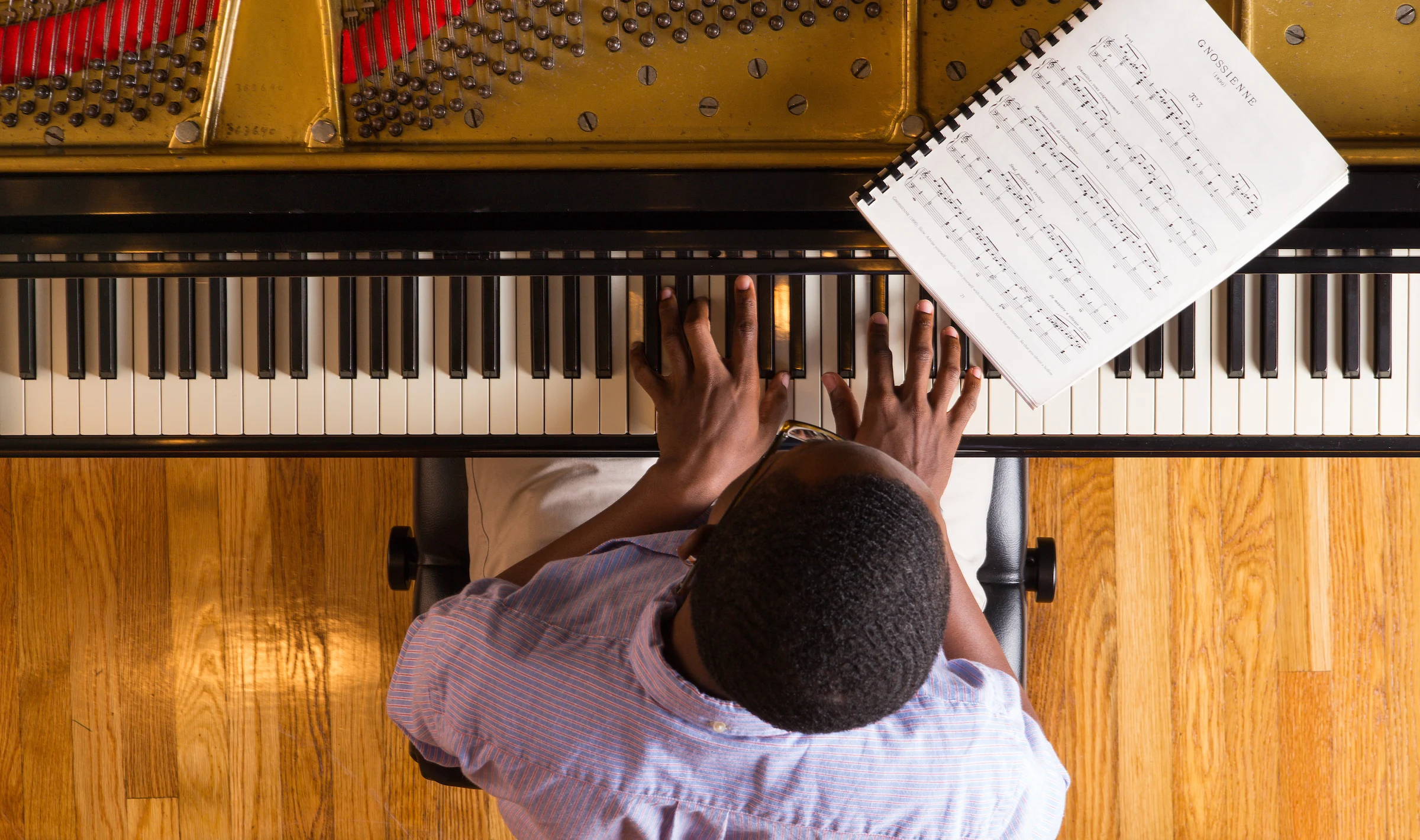 A person plays piano with sheet music, viewed from above on a wooden floor—perfect inspiration for those seeking Music Scholarships.