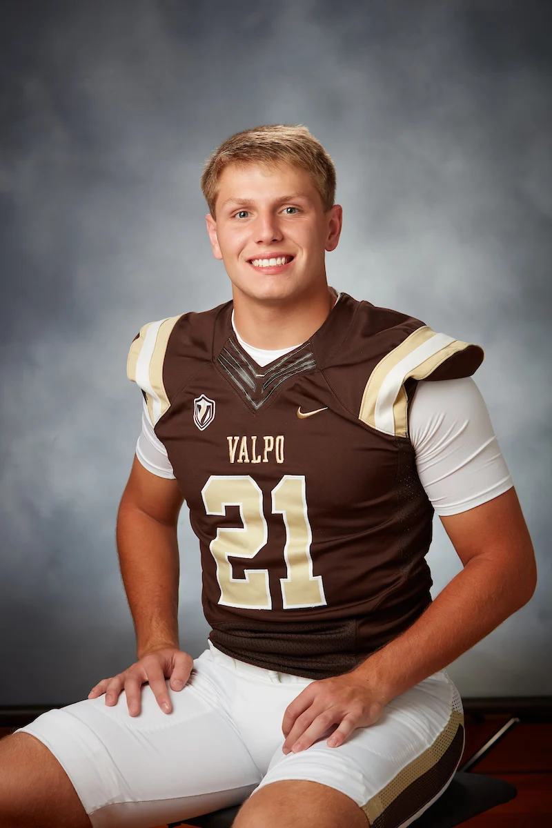 Young athlete in a brown and white football uniform with number 21, sitting and smiling at the camera.