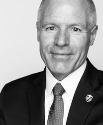 Smiling man in a suit and tie, wearing a lapel pin, in a black and white portrait—President Heckler thoughtfully poses before making a statement on the Indiana Religious Freedom Restoration Act.