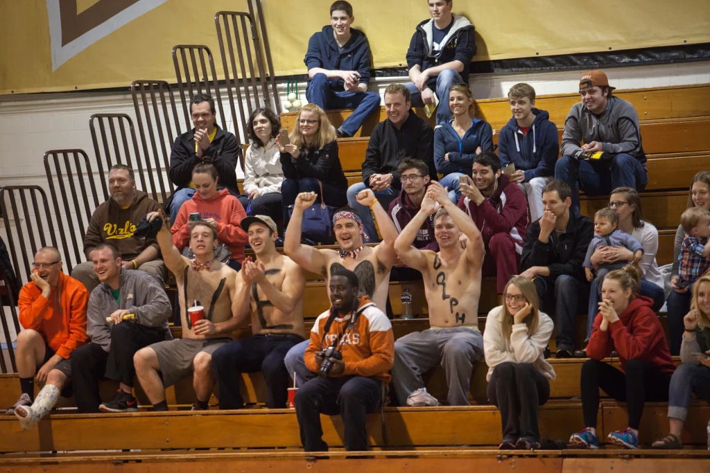 Excited crowd on bleachers; shirtless young men in front cheer at an indoor sports event, as Valpo faces Purdue Kokomo in a thrilling match of ROBOT FOOTBALL.