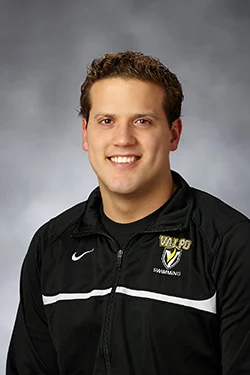 Smiling man, Fernando Aguilar, in a black Valpo swimming jacket against a gray studio background.