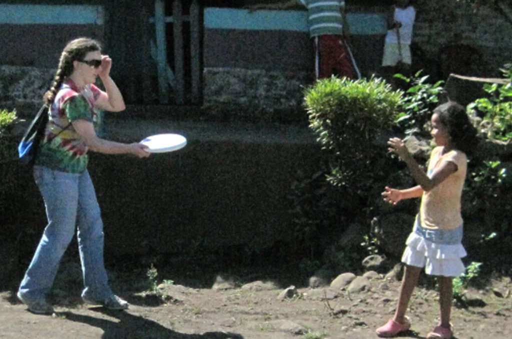An adult and a child play with a white frisbee outside on a sunny day.