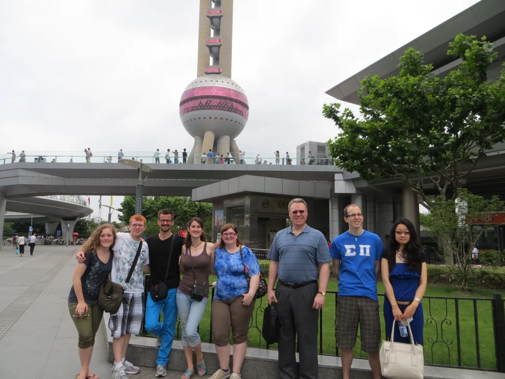 A group of people posing in front of the Oriental Pearl Tower in Shanghai on a cloudy day, making history in Shanghai with their memorable gathering.