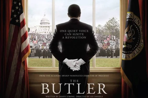 A man in a suit stands facing the White House, with protestors and flags visible through a large window—a scene reminiscent of movie history moments depicted in The Butler.