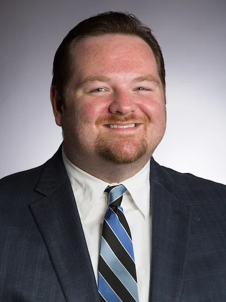 Smiling man in a suit and striped tie, posing against a plain gray background, represents Wheat Ridge Ministries and highlights new research opportunities.