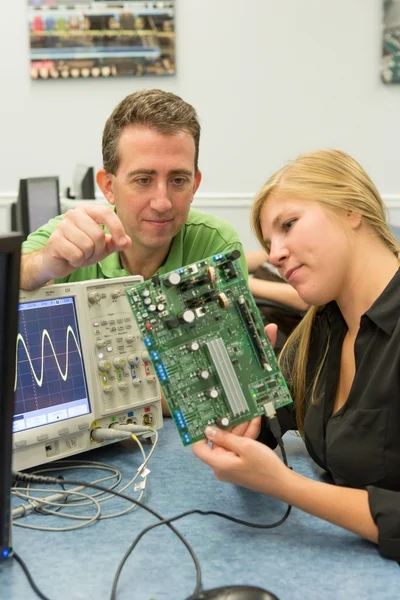Two students from Valpo Engineering examine a circuit board next to an oscilloscope displaying a waveform, exploring practical skills from their new course.