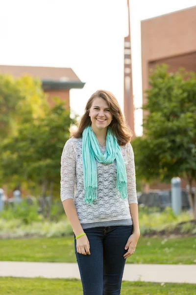 Young Valpo Engineering student in a blue scarf smiles while standing outside on a sunny day, with buildings and greenery behind her, passionate about environmental remediation.