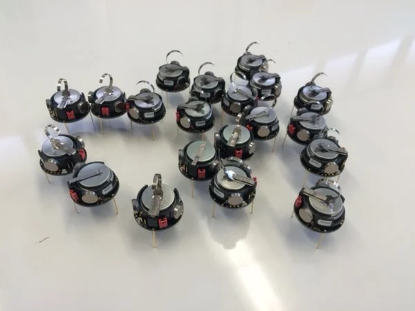 A group of small, round robots with metallic tops and legs arranged on a white surface showcases Swarm Robotics, highlighting innovations in emerging technologies at Valparaiso University.