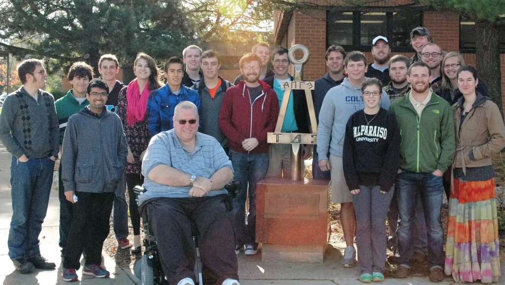 A group of people smiling and posing together outdoors next to a large metal sculpture, representing the camaraderie of the Tau Beta Pi Engineering Honor Society.