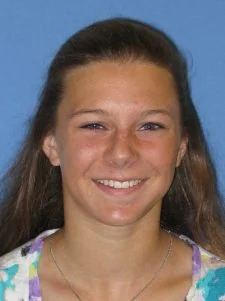 Smiling young woman with long brown hair against a blue background.
