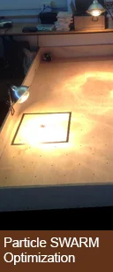 A tabletop research experiment setup under lamps, labeled "Particle SWARM Optimization" at the bottom.