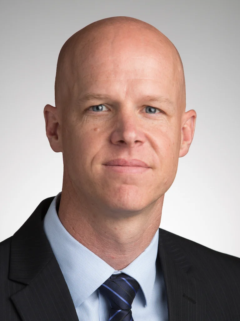 A bald man in a suit and tie poses against a neutral background, looking directly at the camera, featured in this CC Faculty News update.