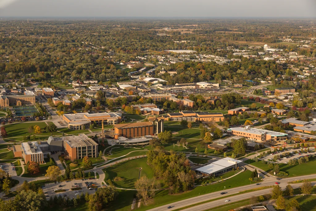 Aerial view of a college campus with several buildings, roads, and green spaces surrounded by trees and neighborhoods, showcasing the Launch of the Aviation Program in Fall 2017.