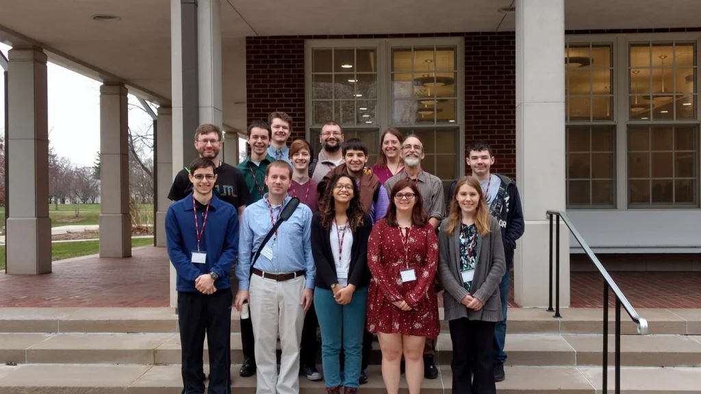 A group of fifteen students and MST faculty pose and smile together on steps outside a building with large windows at a statewide conference.