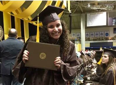 A smiling graduate in cap and gown holds up her diploma at a graduation ceremony, truly prepared for success.