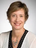Prof. Belanger, a woman with short light brown hair, wearing a black top with a white cardigan, smiles at the camera during the interview.