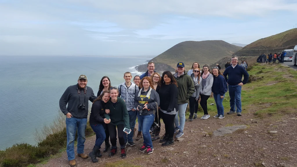 A group of Students Abroad pose on a coastal cliffside with the ocean and hills in the background.