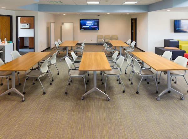 Modern meeting room at Valparaiso University with movable tables and chairs arranged in a U-shape, facing a wall-mounted TV—ideal for collaboration in this Innovation Hub.