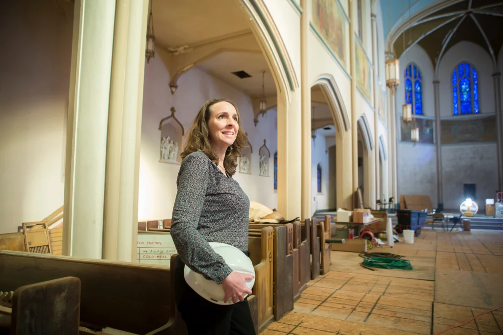 A Valpo Alum holding a hard hat stands inside a church under renovation, surrounded by tools and materials, building a solid foundation to make a world of difference.