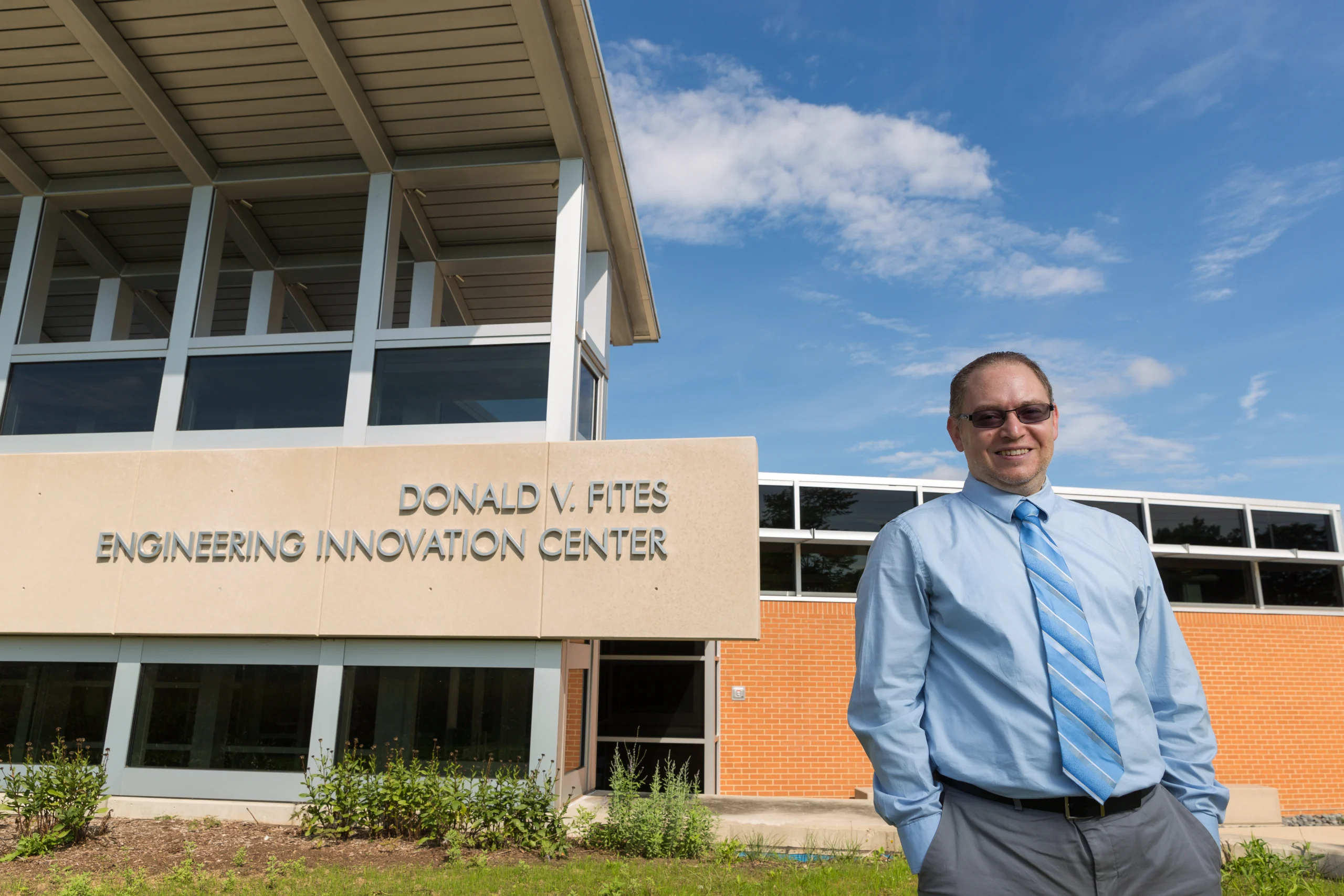 Man in a blue shirt stands smiling outside the Donald V. Fites Engineering Innovation Center, where Valpo Professors are honored for their Excellence in Teaching.
