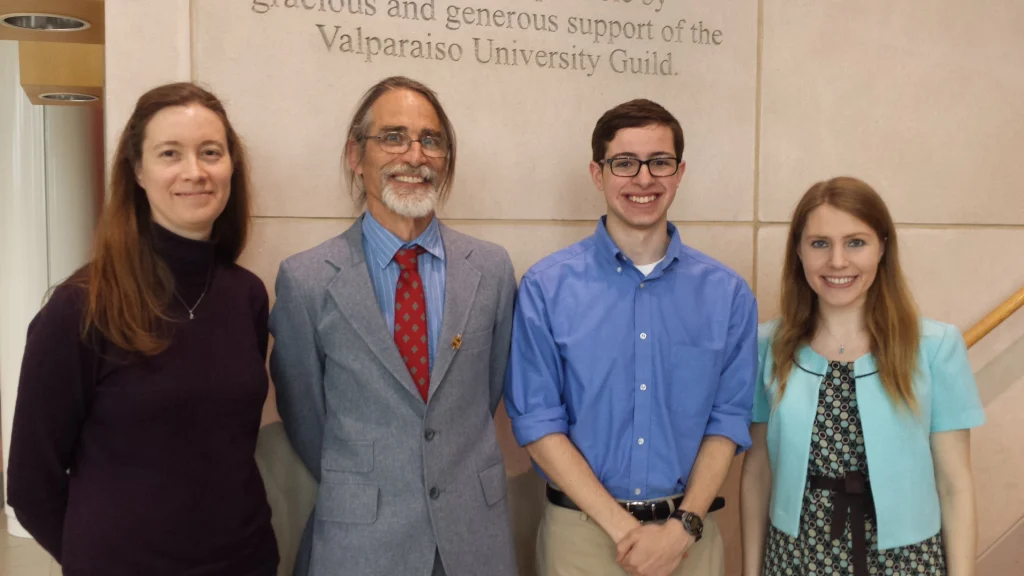 Four people stand smiling in front of a wall with "Valparaiso University Guild" text, including Sam Iselin, a Math major and proud member of Phi Beta Kappa.