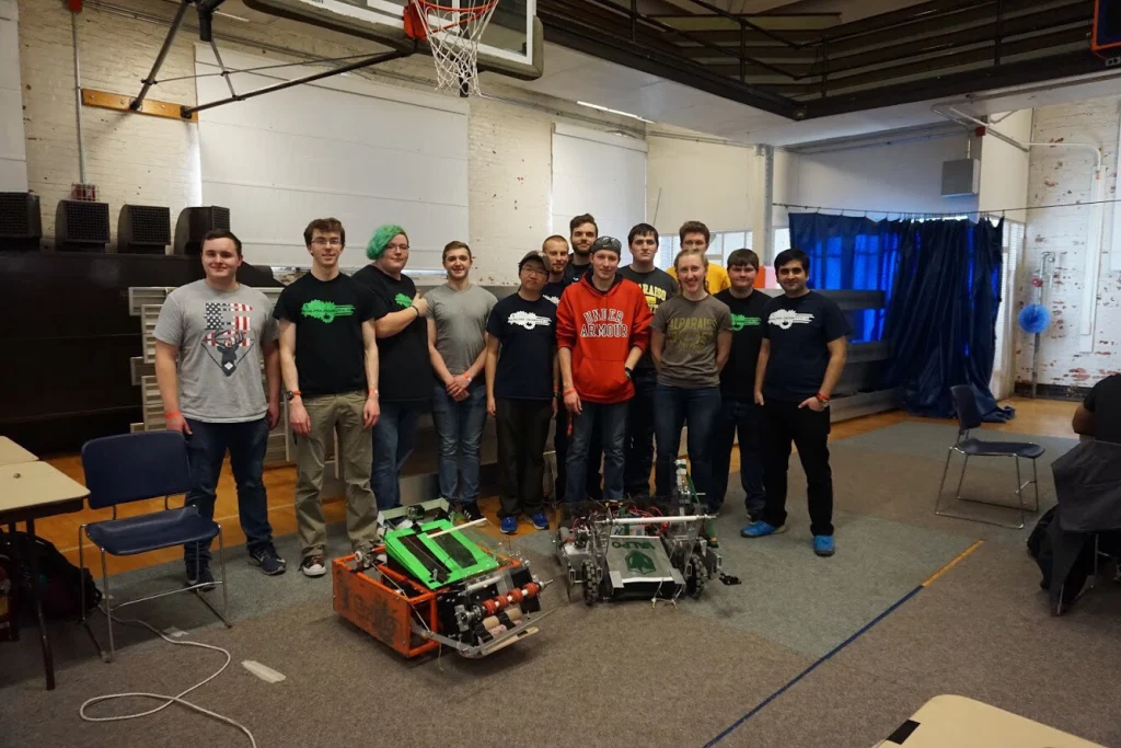 A group of students from Valpo Robotics poses indoors with two large robots in front of them after earning Top Honors at a recent Design Competition.