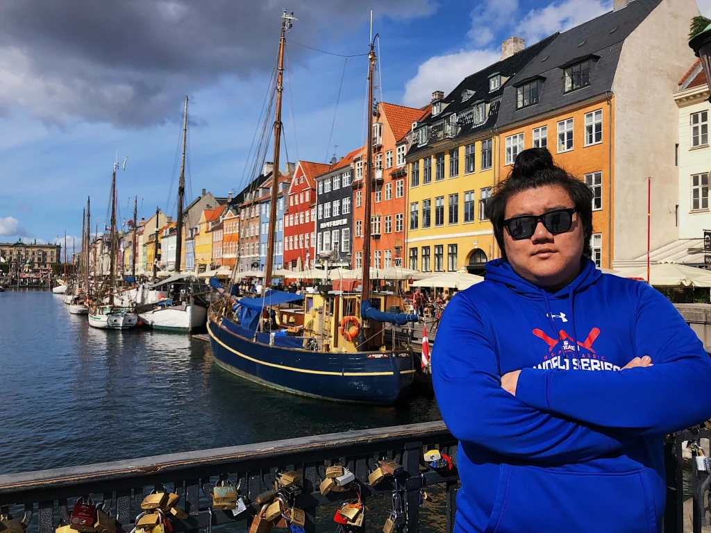COE students enjoy a new experience as one stands in a blue hoodie and sunglasses by a canal, with colorful buildings and boats in the background.