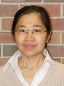 A woman wearing glasses and a white collared shirt stands in front of a brick wall, smiling slightly—one of many dedicated Valpo Faculty Members known for their commitment to excellence.