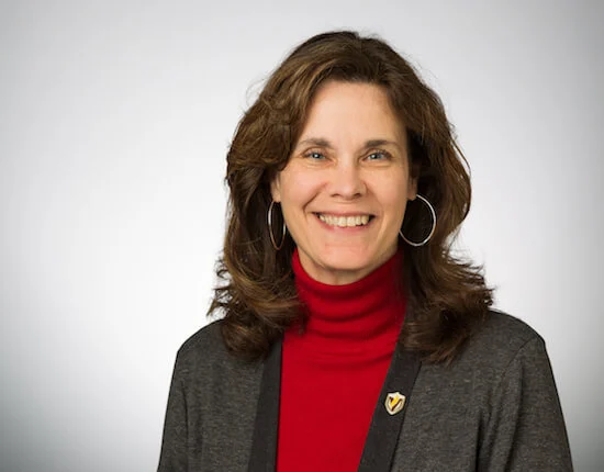 Smiling woman with wavy brown hair, wearing a red turtleneck and dark blazer, posing against a light background as the Dean of Library at Valparaiso University.
