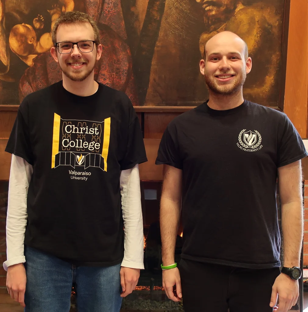 Two young men smiling, both Orr Fellows and alumni of Valparaiso University, stand indoors in front of a large painting and a fireplace.