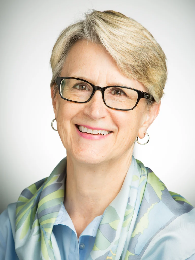 Honored Valpo Professor, a smiling older woman with short blond hair, glasses, and a light blue scarf over a blue shirt, recognized for her Excellence in Teaching.