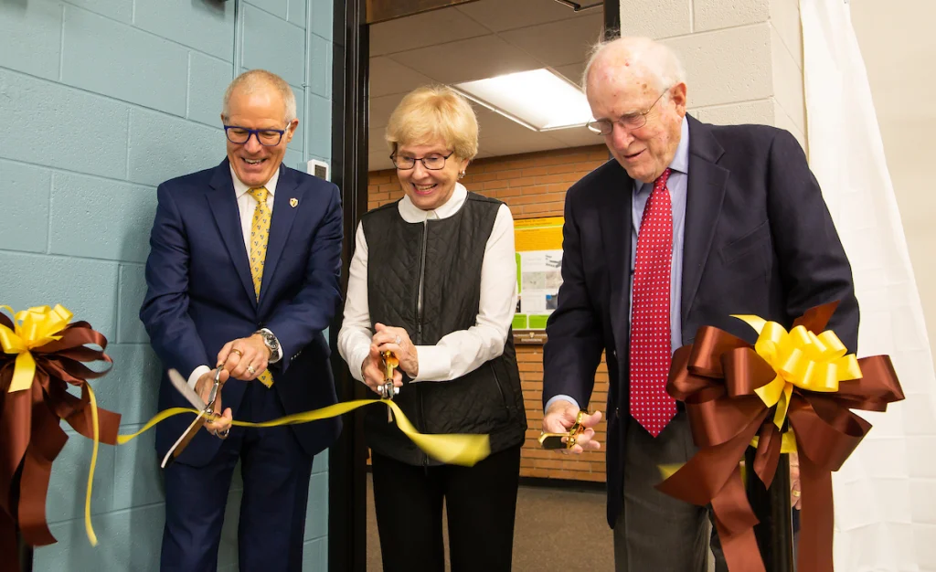 Three people smiling and cutting a yellow ribbon with large scissors at the Environmental Engineering Lab dedication ceremony.