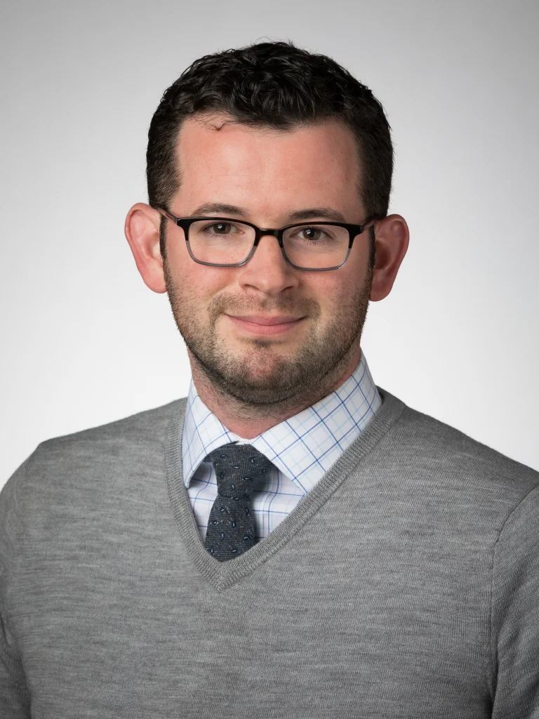 A man wearing glasses, a gray sweater, and a tie, smiling in front of a plain light background, serves as the Endowed Director’s Chair at the Institute for Leadership and Service, Valparaiso University.