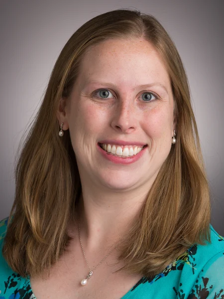 Smiling woman with straight, light brown hair and blue eyes, wearing a teal top and pearl jewelry, poses confidently as a MAA representative.