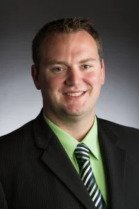 Smiling man in a suit, green shirt, and striped tie against a dark background—Kevin Steele, SEAC Employee of the Month for April 2020.