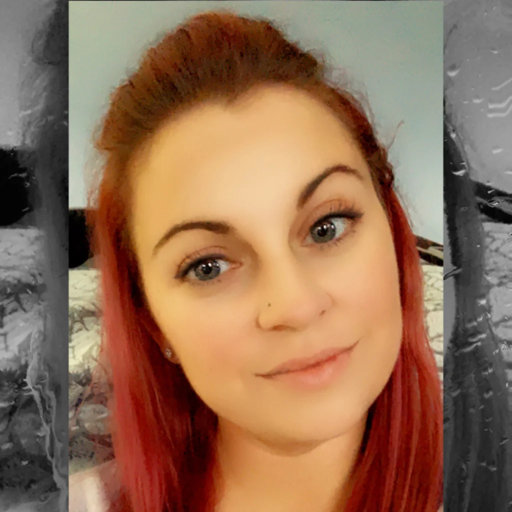 A woman with long red hair and a nose piercing, smiling softly at the camera, is one of the proud Members of the 2020 Class.