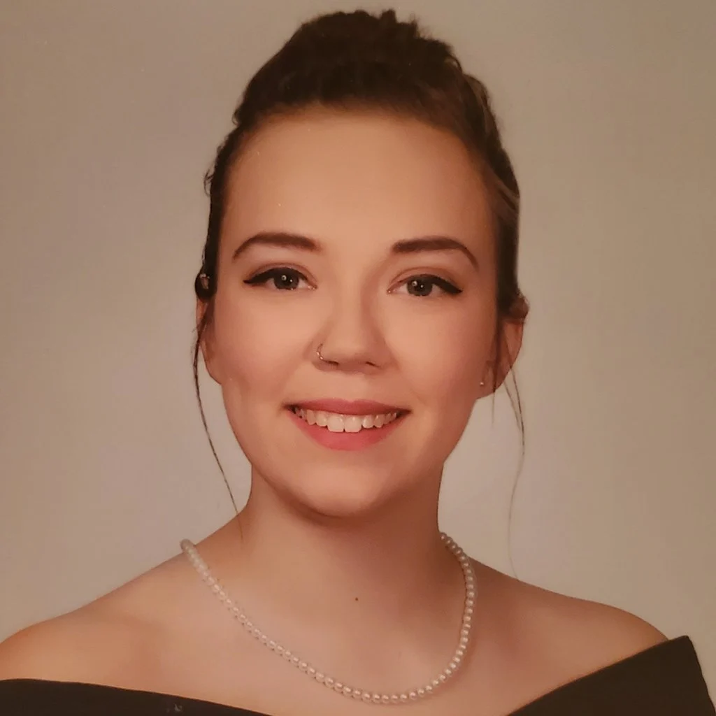 Smiling woman, a member of the 2020 Class, in a black off-shoulder top and pearl necklace with hair in a neat bun.