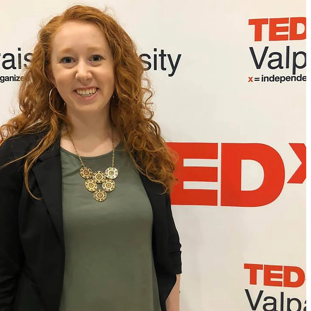 Woman with red hair smiling in front of a TEDx Valparaiso University event backdrop, celebrating with fellow 2020 Class members.