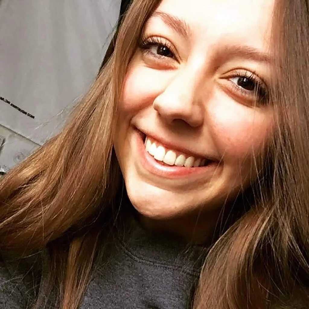 Young woman with long brown hair smiling brightly, wearing a dark top, close-up selfie; a proud member of the 2020 Class.