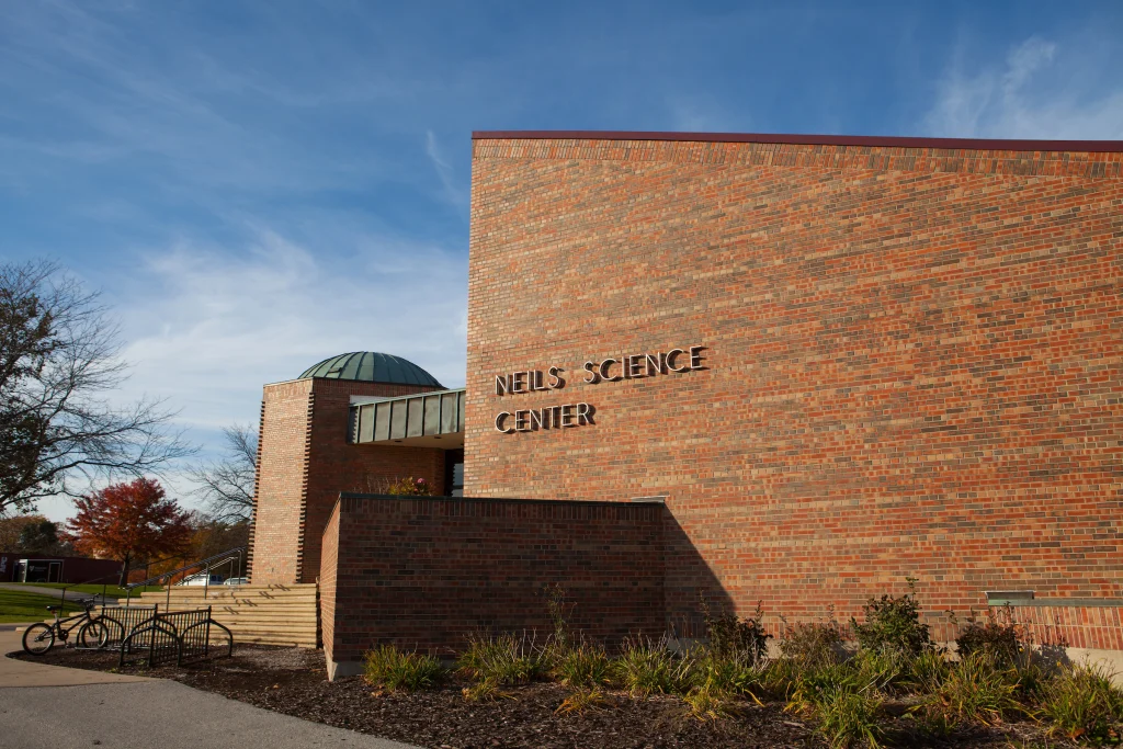 A brick building with "Niels Science Center" on the wall under a blue sky at Valparaiso University, where bikes are parked nearby and cutting-edge Physics Research is conducted.