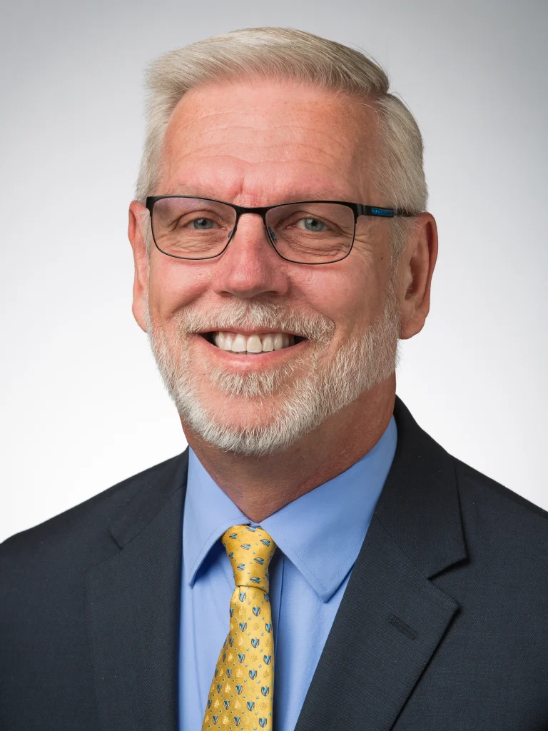 Smiling older man with gray hair, glasses, and beard, wearing a suit, blue shirt, and yellow patterned tie—depicted as a confident member of an Incident Command Team.