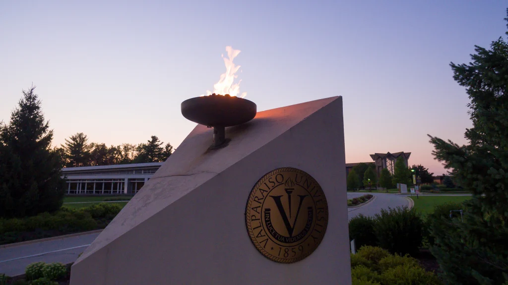 A flame burns atop a monument with the Valparaiso University seal at sunset, celebrating the impact of a $1 Million Grant from the Lilly Endowment.