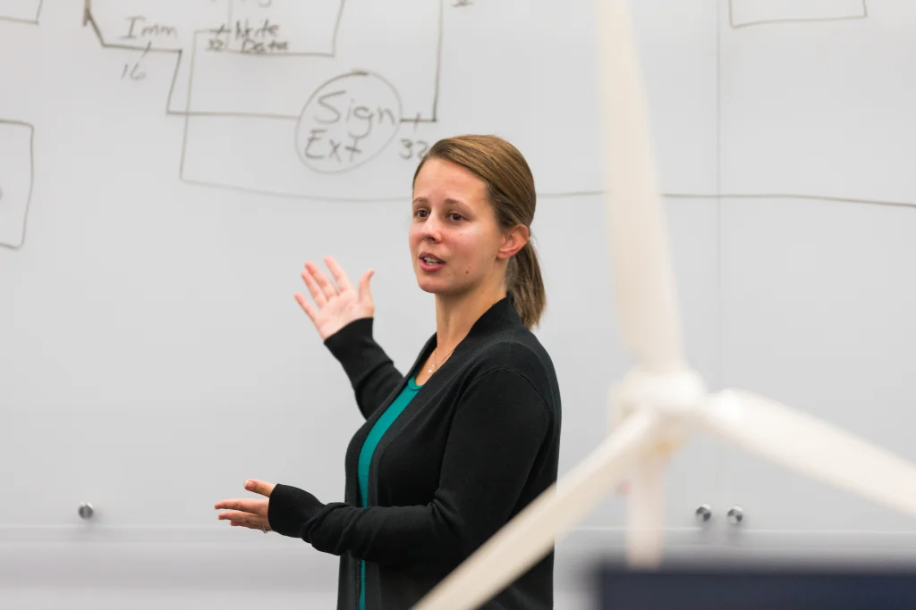 Jenny Marley presents in front of a whiteboard with diagrams, next to a model wind turbine in the foreground, highlighting her teaching recognition after receiving the Outstanding Teaching Award.