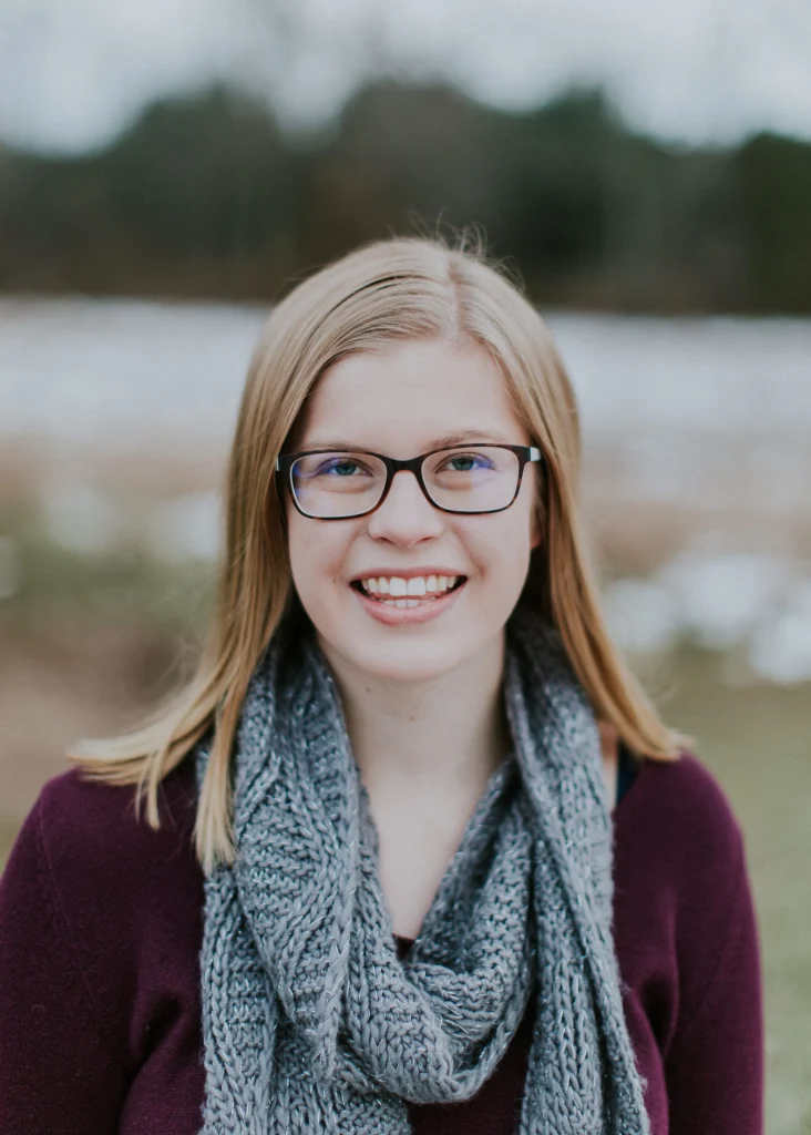 Young woman with glasses and a gray scarf, among fellow Valpo Students, smiles outdoors on a cloudy day.