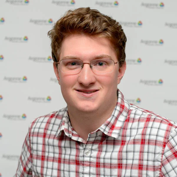 A person wearing glasses and a red plaid shirt smiles in front of a patterned background, representing the spirit of Valpo Students.