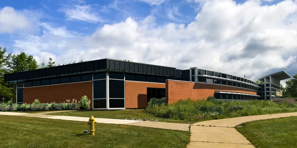 Modern brick and glass building with lawns, sidewalk, and a yellow fire hydrant under a partly cloudy sky—an inspiring home for bioengineers, complete with a dedicated lab inside.