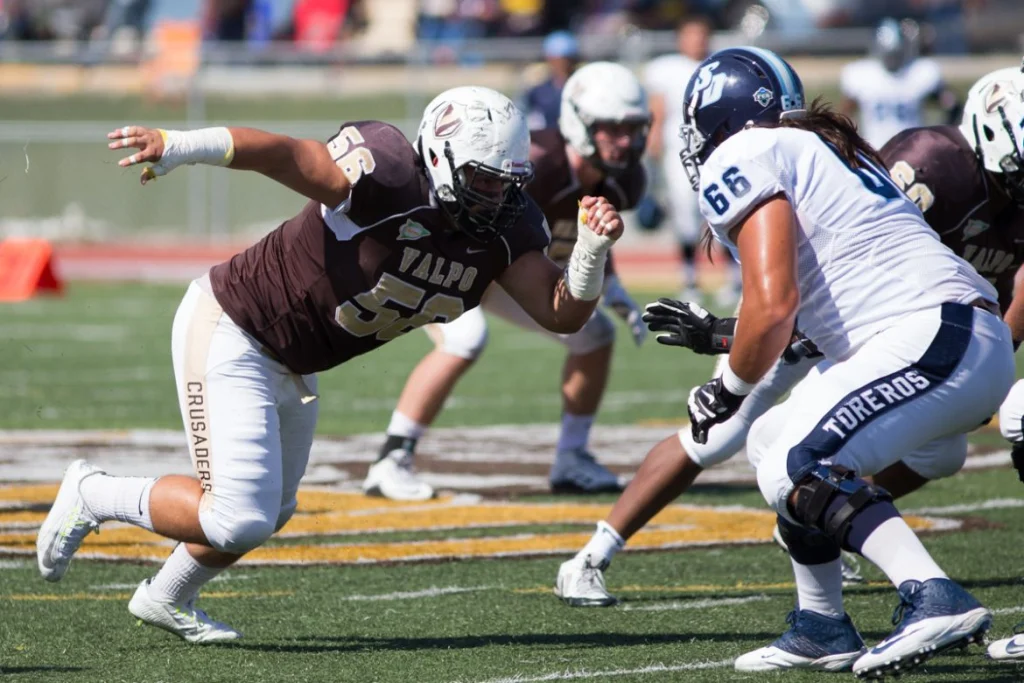 Valpo Student-Athletes show determination as a football player rushes towards a Toreros opponent during a game on a sunny day.