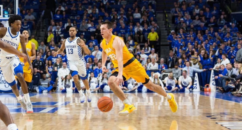 A basketball player in yellow dribbles the ball while Valpo Student-Athletes in white defend on a crowded court.