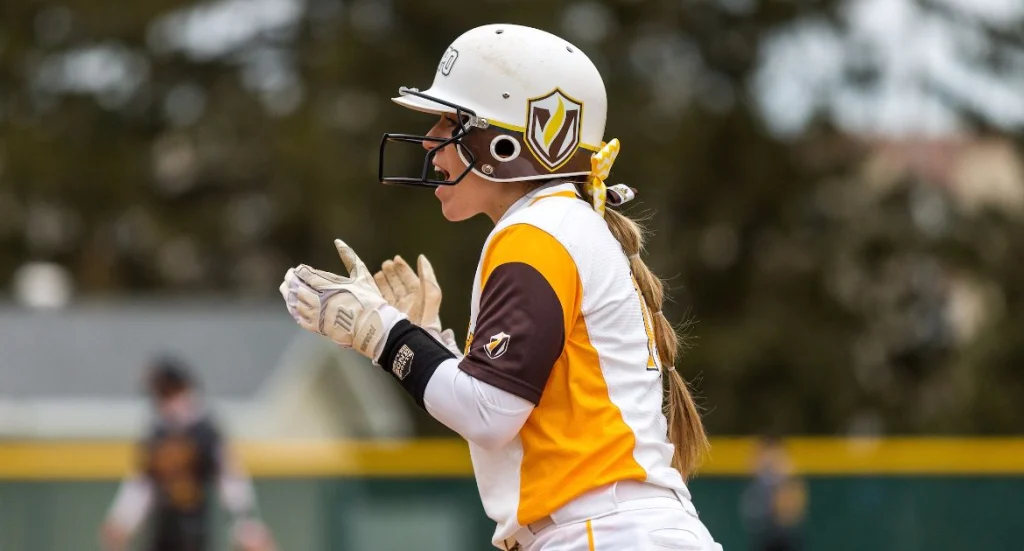A Valpo student-athlete in yellow and white claps her hands and cheers while wearing a helmet and gloves, celebrating the spirit shown by frontline workers during COVID-19.